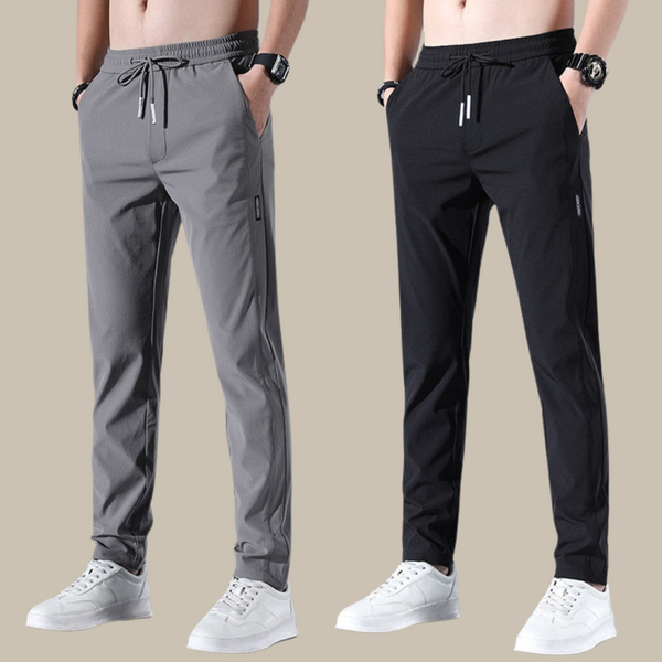 Twee heren joggingbroeken, grijs en zwart, met elastische tailleband en trekkoord, gedragen met witte sneakers. Comfortabele sportkleding.
