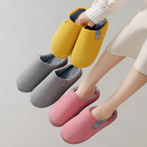 Drie paar pantoffels in geel, grijs en roze met zachte voering, gedragen door een persoon. Comfortabele huisschoenen voor dames.