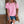 Vrouw in roze geperforeerd T-shirt en denim shorts, met bruine schoudertas en koffiehouder, tegen witte bakstenen muur. Zomermode, casual outfit.
