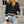 Vrouw in zwarte trui met witte strepen en ritssluiting, gecombineerd met lichtblauwe jeans. Modieuze casual outfit voor dames.