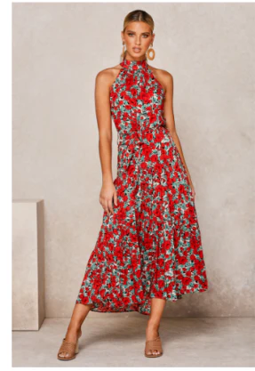Vrouw in rode bloemenjurk met halternek, staand tegen neutrale achtergrond. Zomerse mode, elegante dameskleding, trendy jurk.