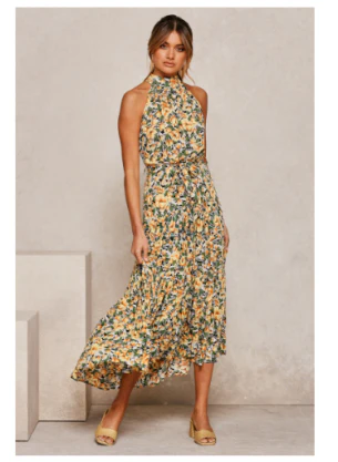 Vrouw in elegante, lange bloemenjurk met halternek, gele en groene print. Perfect voor zomermode, casual en feestelijke gelegenheden.