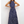 Vrouw in blauwe maxi-jurk met witte bloemenprint, mouwloos en hoge hals, poseert tegen witte achtergrond. Trendy damesmode, zomerjurk.