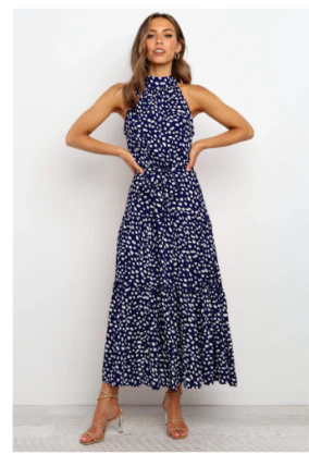 Vrouw in blauwe maxi-jurk met witte bloemenprint, mouwloos en hoge hals, poseert tegen witte achtergrond. Trendy damesmode, zomerjurk.
