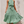 Vrouw in groene polkadot zomerjurk met halternek en strikceintuur, poseert tegen een neutrale achtergrond. Perfecte outfit voor zomermode.