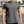 Man in grijs T-shirt met korte mouwen en zilveren ketting, gespierde armen, buiten gefotografeerd. Casual herenkleding, fitnessmode.