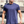 Man in donkerblauw T-shirt met ketting, gespierde armen, buitenomgeving. Casual herenkleding, fitnessmode, stedelijke achtergrond.