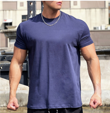 Man in donkerblauw T-shirt met ketting, gespierde armen, buitenomgeving. Casual herenkleding, fitnessmode, stedelijke achtergrond.