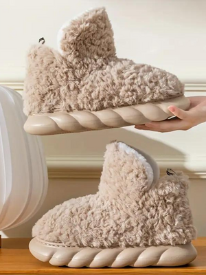 Beige pluche pantoffels met dikke, gewatteerde zolen op houten oppervlak. Comfortabele, warme slippers voor binnengebruik. Trendy en knus design.