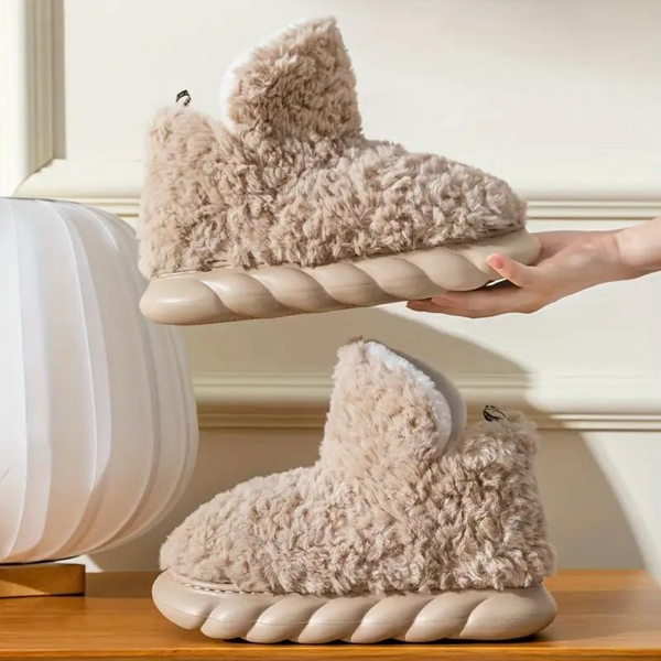 Beige pluche pantoffels met dikke, gewatteerde zolen op houten oppervlak. Comfortabele, warme slippers voor binnengebruik. Trendy en knus design.