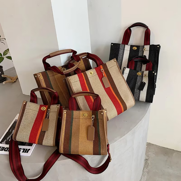 Vijf gestreepte handtassen met rode handvatten op een witte tafel, gemaakt van canvas. Modieuze damesaccessoires, perfect voor dagelijks gebruik.