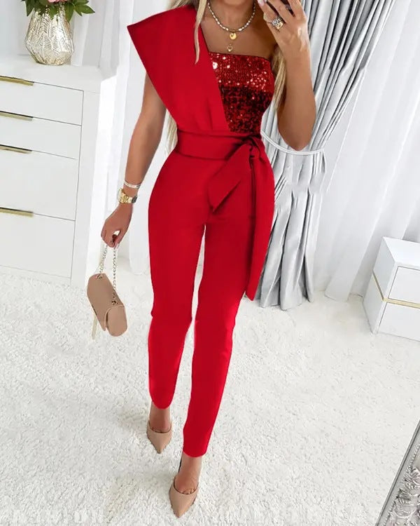 Rode jumpsuit voor dames met asymmetrisch ontwerp en pailletten top, gecombineerd met beige hakken en handtas. Perfect voor feestelijke gelegenheden.