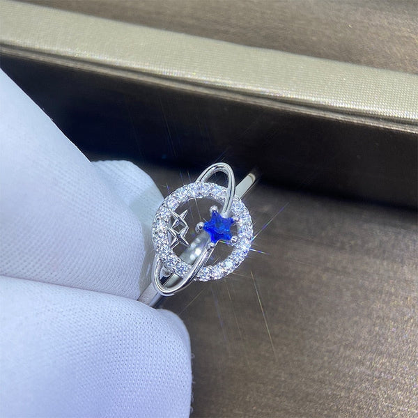 Zilveren ring met blauwe ster en cirkelvormig ontwerp, ingelegd met diamanten, gepresenteerd in een luxe doos. Perfect als elegante sieradenkeuze.