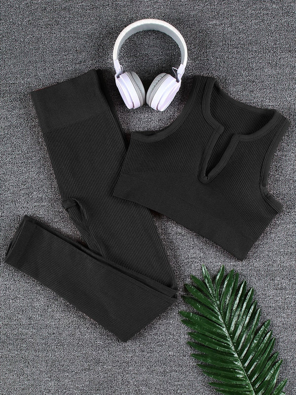 Zwarte sportlegging en crop top set met witte koptelefoon op grijze achtergrond, naast groene palmblad. Perfect voor yoga en fitness.
