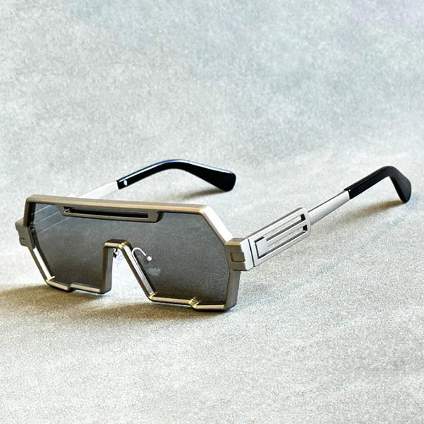 Zilveren futuristische zonnebril met rechthoekige glazen en zwarte pootjes op grijze achtergrond. Trendy unisex accessoire, moderne stijl.