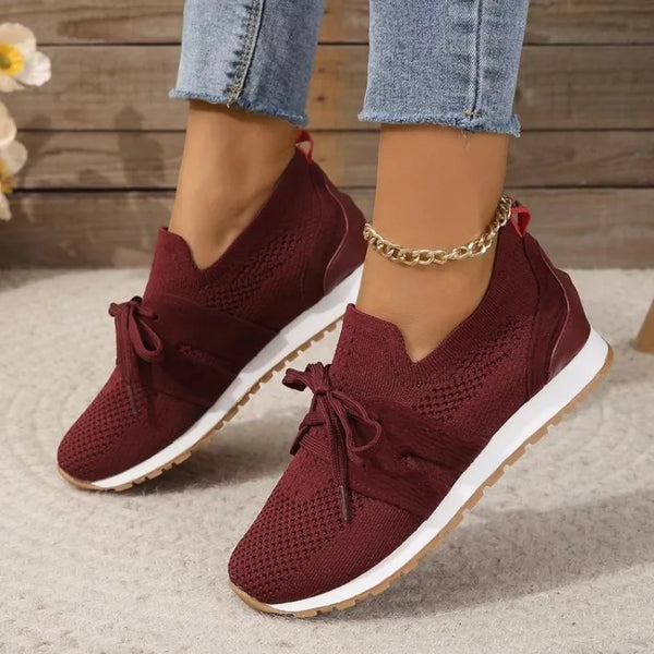 Bordeauxrode dames sneakers met gebreid bovenwerk, witte zool en veters, gedragen met blauwe jeans. Comfortabele en modieuze schoenen.