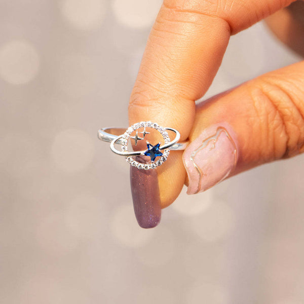 Zilveren ring met blauwe stersteen en cirkelvormig ontwerp, vastgehouden door hand met gelakte nagels. Elegante sieraden voor dames.