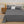 Grijs beddengoed set op tweepersoonsbed met kussens, naast houten nachtkastje met zonnebloemen en decoratieve items, moderne slaapkamer inrichting.