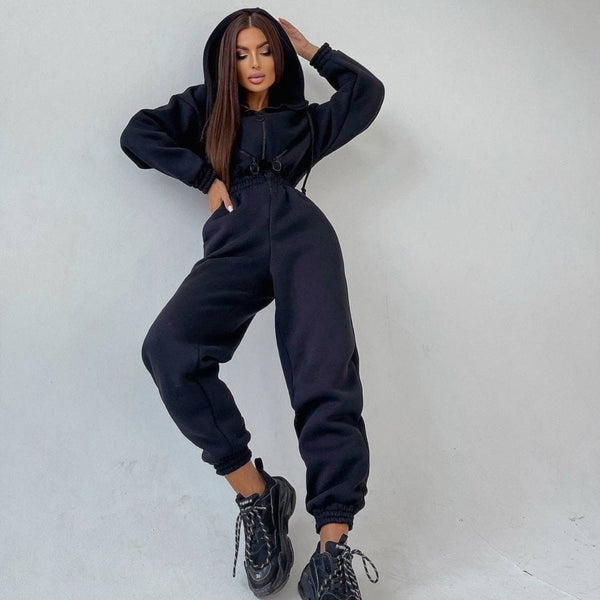 Vrouw in zwarte hoodie en joggingbroek poseert tegen witte achtergrond, draagt chunky sneakers. Modieuze streetwear outfit, casual stijl.