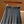 Grijze geplooide rok met zwarte riem, hangend aan houten hanger. Modieuze dameskleding, ideaal voor kantoor of casual outfits.