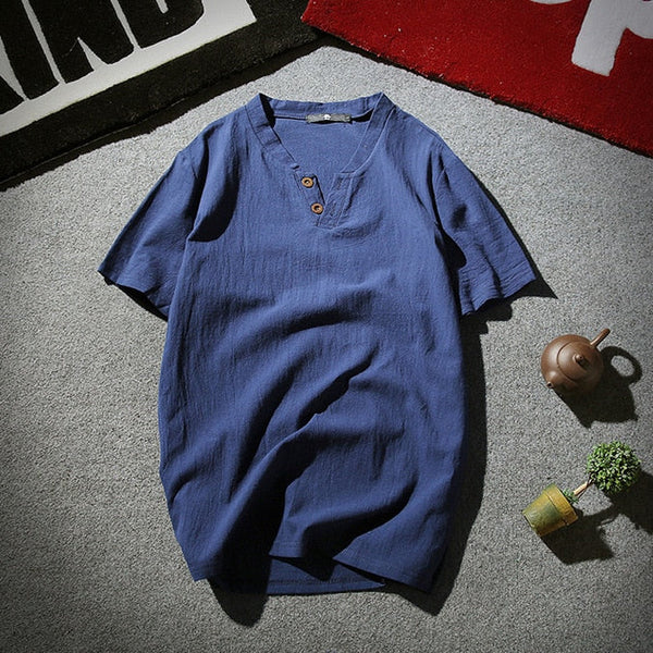 Blauw linnen heren T-shirt met korte mouwen en knoopsluiting, casual stijl, op grijze vloer met theepot en plantdecoratie.