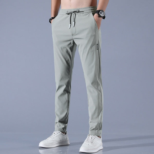 Lichtgrijze sportbroek voor heren, met elastische tailleband en trekkoord, gecombineerd met witte sneakers. Comfortabele en stijlvolle sportkleding.