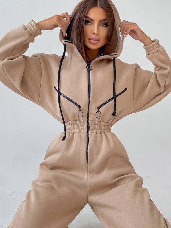 Vrouw in beige jumpsuit met capuchon en zwarte trekkoorden, modieuze streetwear, comfortabele pasvorm, trendy kledingstijl, casual outfit.