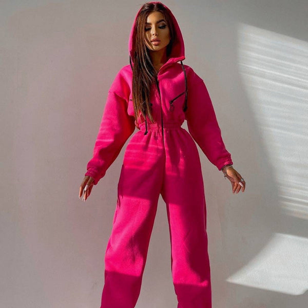 Vrouw in felroze joggingpak met capuchon, poseert tegen een neutrale achtergrond. Modieuze dameskleding, comfortabele loungewear, trendy outfit.