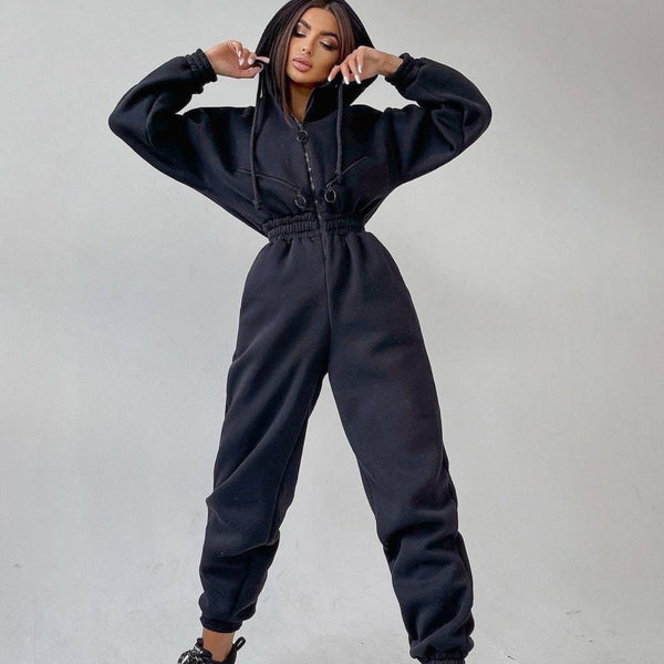 Vrouw in zwarte jumpsuit met capuchon, comfortabele mode, casual streetwear, trendy dameskleding, sportieve outfit, minimalistisch design.