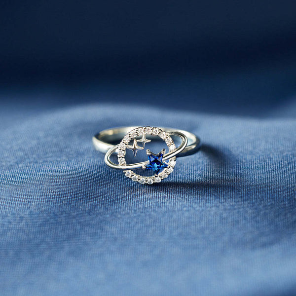 Zilveren ring met blauwe ster en zirkonia, geïnspireerd op planeten en sterren, op blauwe achtergrond. Perfect als elegante sieradenaccessoire.