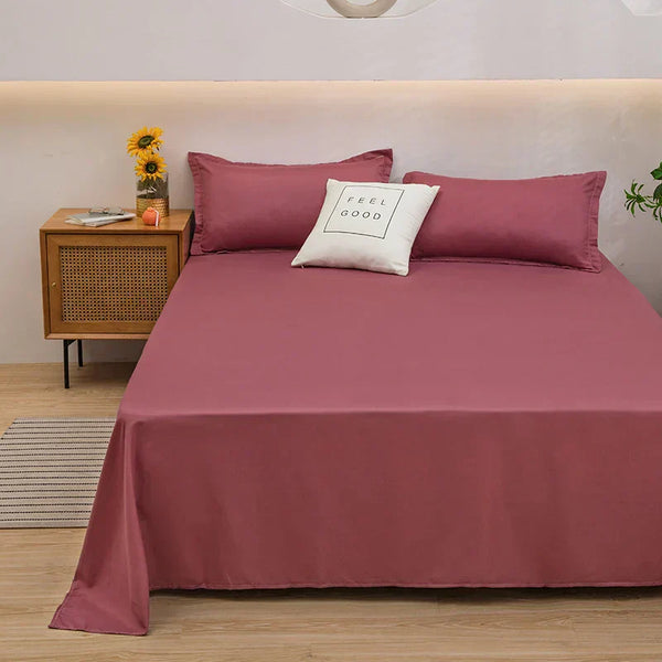 Roze beddengoed set met kussens op een tweepersoonsbed, naast een houten nachtkastje met zonnebloemen en een decoratief kussen met "Feel Good" tekst.