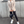 Vrouw in beige blazer en zwarte leren legging met witte sneakers en zwarte schoudertas, modieuze straatstijl, stedelijke achtergrond.