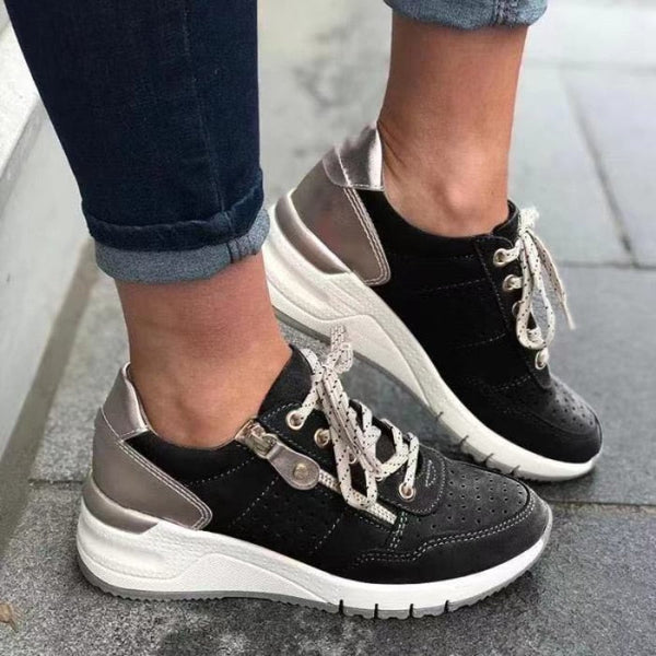Zwarte en witte sneakers met metallic details en veters, gedragen door een persoon op een stoep. Modieuze dames sneakers, casual stijl.