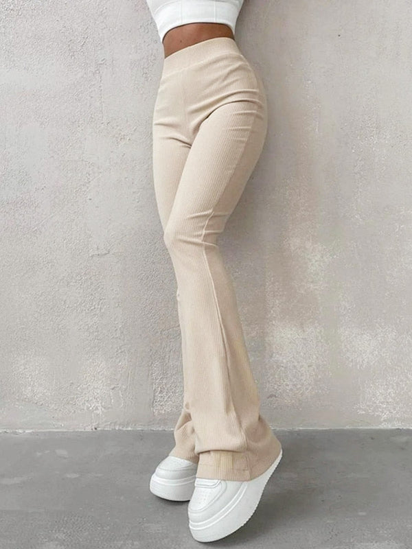 Vrouw in beige flared broek en witte sneakers tegen een grijze achtergrond. Modieuze dameskleding, trendy broeken, casual outfit.
