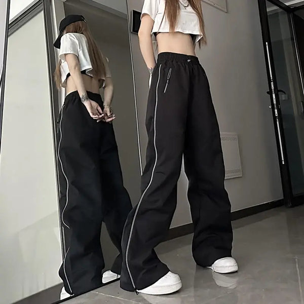 Vrouw in zwarte wijde broek met witte strepen, crop top en pet, poseert voor spiegel. Trendy streetwear mode, casual outfit, moderne stijl.