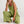 Vrouw in groene linnen jumpsuit met wijde pijpen, zittend op witte achtergrond. Modieuze dameskleding, casual zomeroutfit, comfortabele stijl.