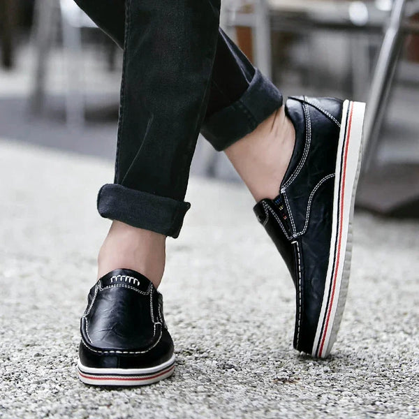 Zwarte leren loafers voor heren met witte en rode zool, gedragen met opgerolde jeans. Stijlvolle casual schoenen voor dagelijks gebruik.