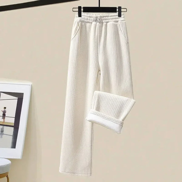 Crèmekleurige geribbelde damesbroek, casual stijl, met elastische tailleband en opgerolde pijpen, hangend aan een zwarte hanger tegen een beige achtergrond.