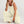 Vrouw in beige jumpsuit met wijde pijpen, zittend op witte achtergrond. Modieuze dameskleding, casual zomeroutfit, trendy stijl.