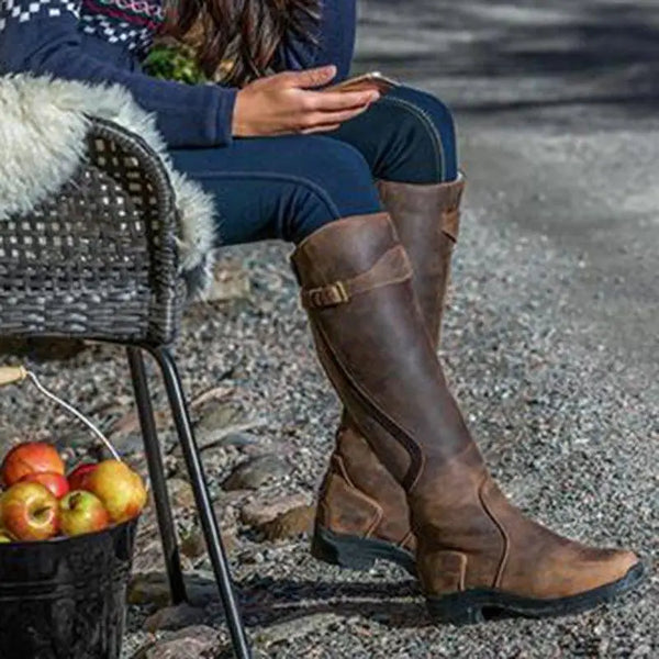 Vrouw met bruine leren laarzen zittend op een stoel buiten, naast een emmer appels. Stijlvolle herfstmode, outdoor laarzen, casual kleding.