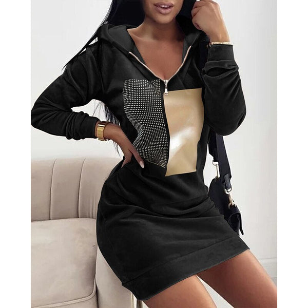 Vrouw in zwarte hoodie-jurk met rits en beige vierkant patroon, zittend op een bank. Modieuze dameskleding, casual stijl, trendy outfit.