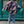 Vrouw in kleurrijke patchwork jas, blauwe jeans en zwarte laarzen loopt op straat. Modieuze winterkleding, stedelijke achtergrond, trendy outfit.