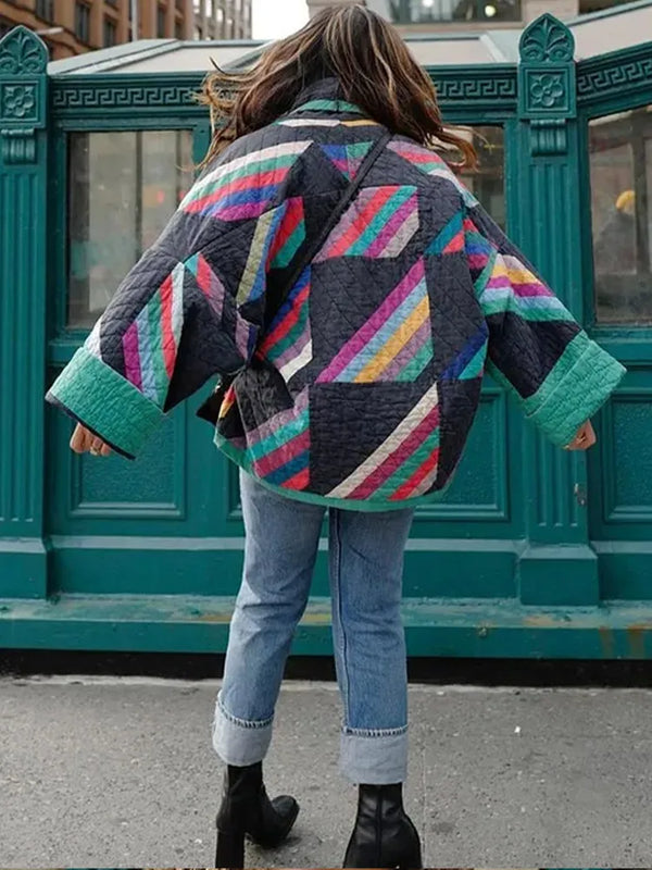 Vrouw in kleurrijke patchwork jas, blauwe jeans en zwarte laarzen loopt op straat. Modieuze winterkleding, stedelijke achtergrond, trendy outfit.