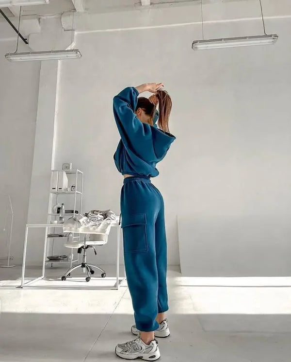 Vrouw in blauwe joggingpak en sneakers in minimalistisch interieur, moderne sportkleding, comfortabele loungewear, casual mode, fitnesskleding.