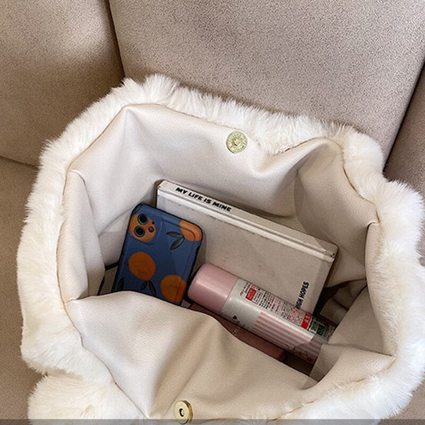 Witte bonttas met binnenin een telefoonhoesje met sinaasappels, notitieboek, roze deodorant en lippenbalsem. Stijlvolle damesaccessoires.