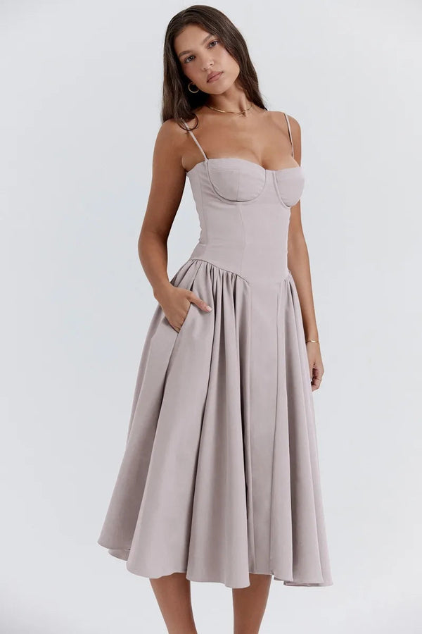 Vrouw in elegante, lichtgrijze midi-jurk met spaghettibandjes en geplooide rok. Perfect voor zomerse evenementen en modieuze gelegenheden.