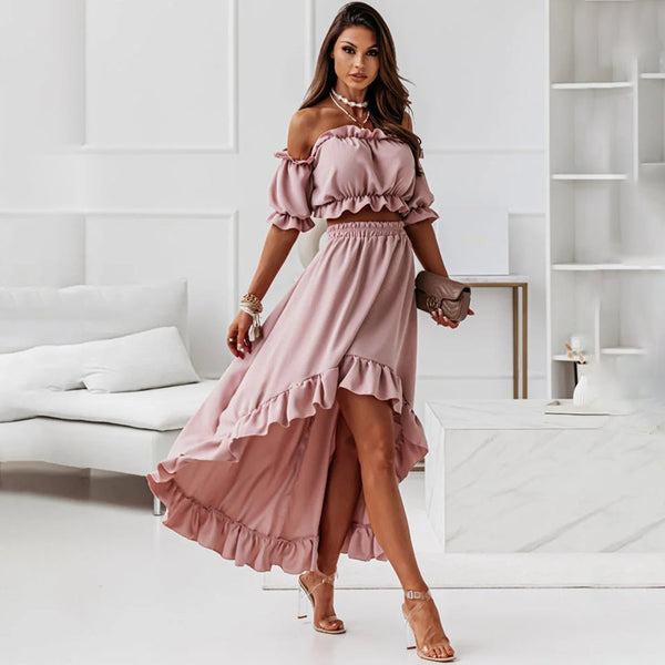 Vrouw in roze off-shoulder jurk met ruches, hoge split en sandalen in moderne woonkamer. Elegante mode, zomerjurk, stijlvolle outfit.