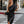 Elegante vrouw in zwarte satijnen asymmetrische jurk, poseert op straat. Modieuze avondkleding, chique stijl, stedelijke achtergrond.
