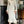 Witte geribbelde midi-jurk met lange mouwen en ruches, gedragen door een vrouw in een klassieke woonkamer. Elegante damesmode, herfstkleding.