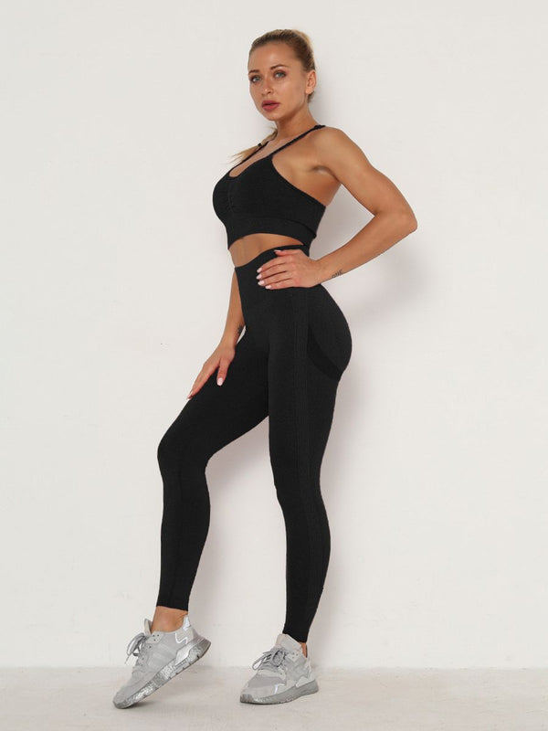 Vrouw in zwarte sportkleding, bestaande uit een sportbeha en legging, poseert tegen een witte achtergrond. Fitnessmode, actieve levensstijl.